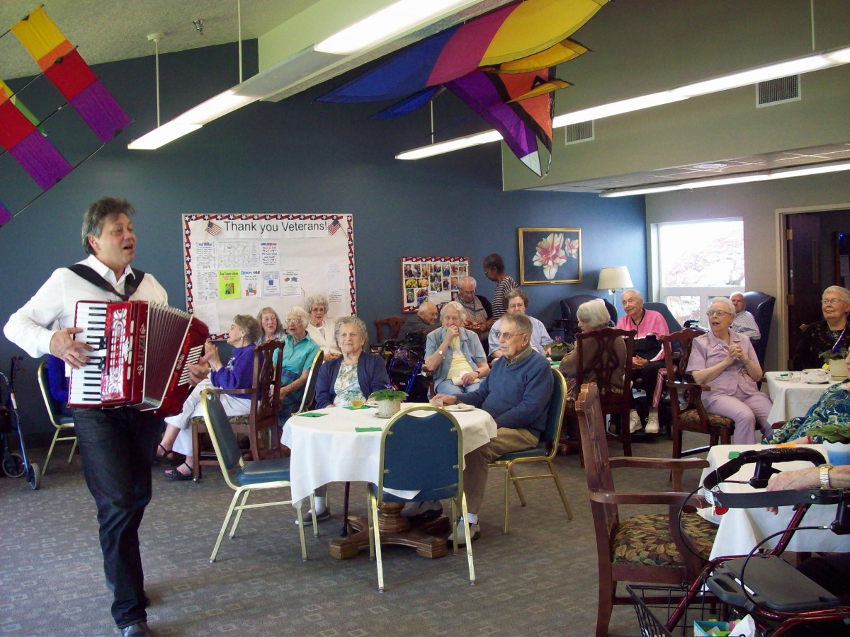 An accordion player performs for an elderly audience at a community event, surrounded by colorful decorations.