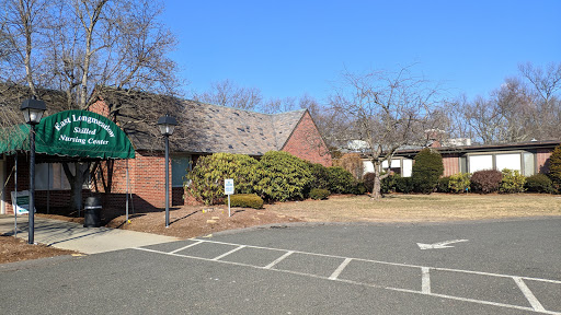 A serene view of a brick building in a parking area, surrounded by trees under a clear blue sky.