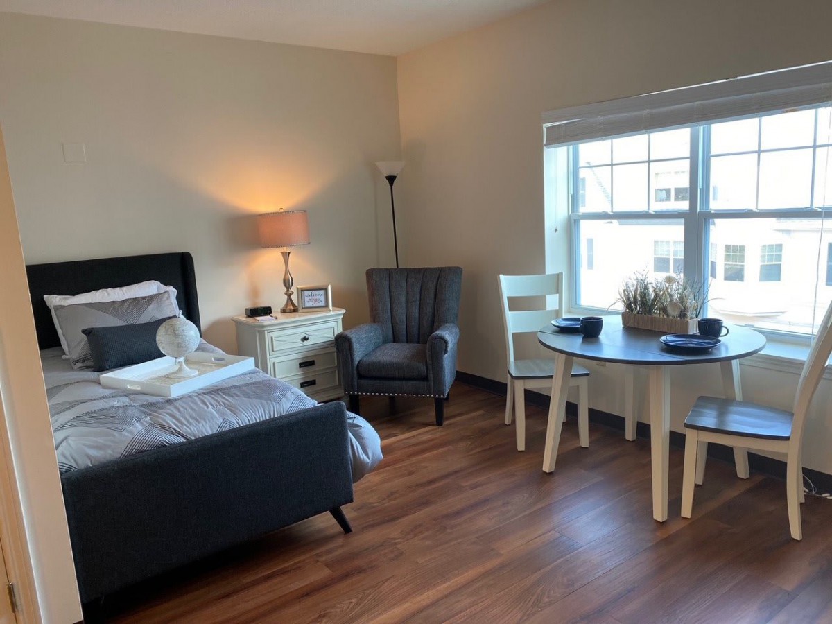 A cozy bedroom with a bed, armchair, and small dining table near a window.