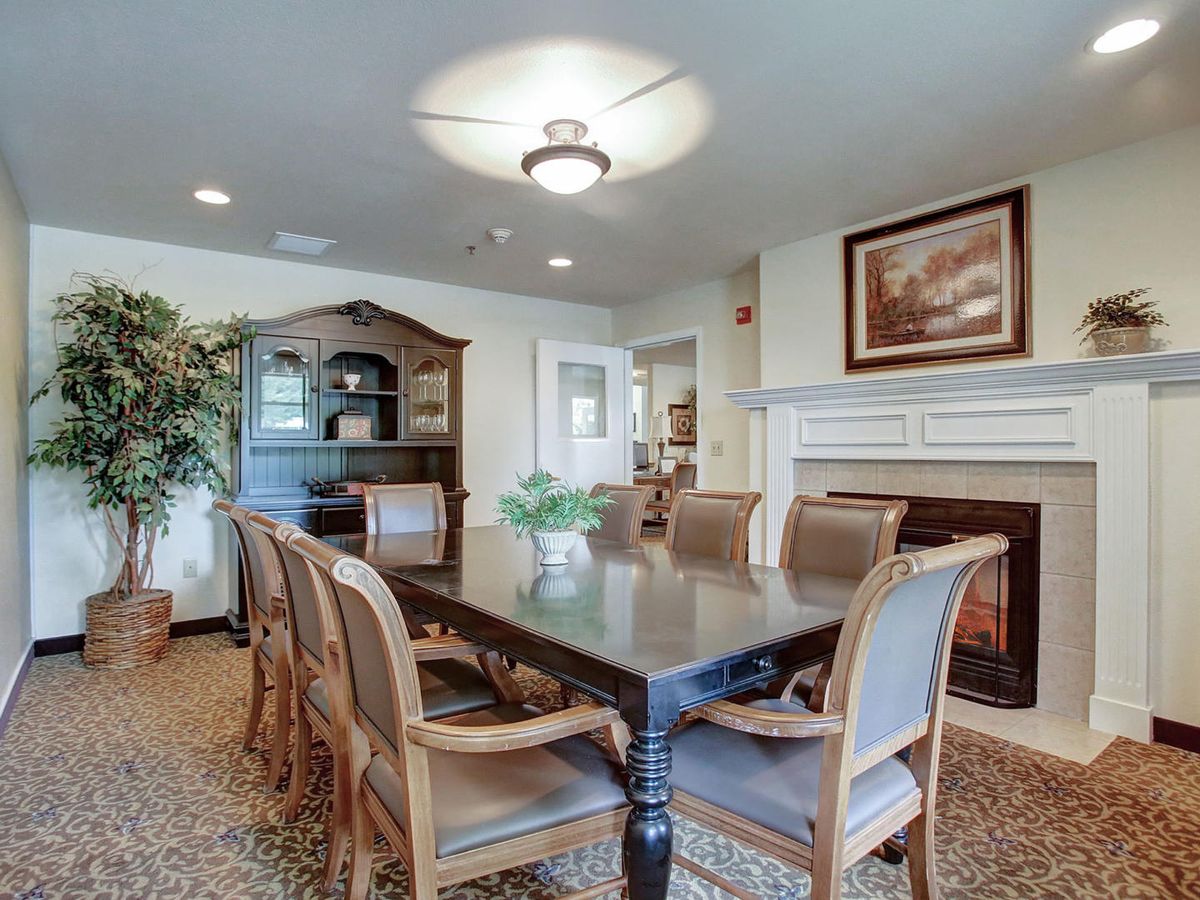 A cozy dining room with a large table, surrounded by chairs and adorned with a chandelier, fireplace, and decorative elements.
