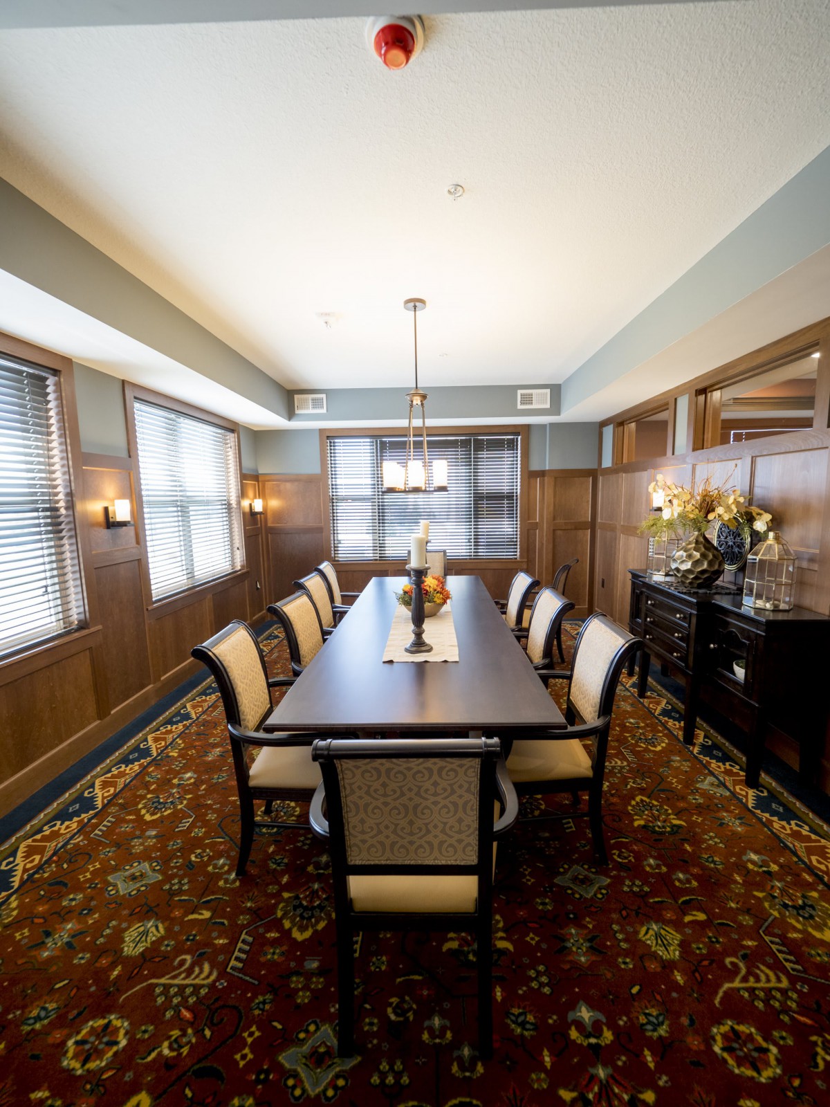 Elegant dining room with a long table, surrounded by chairs and enhanced by wood paneling and decorative lighting.