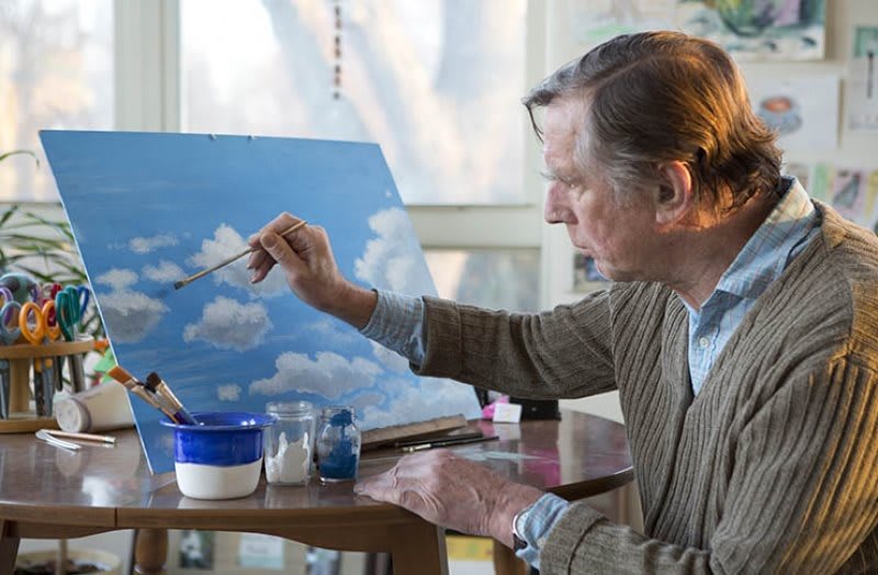 An artist in their studio working on a sky-themed painting.