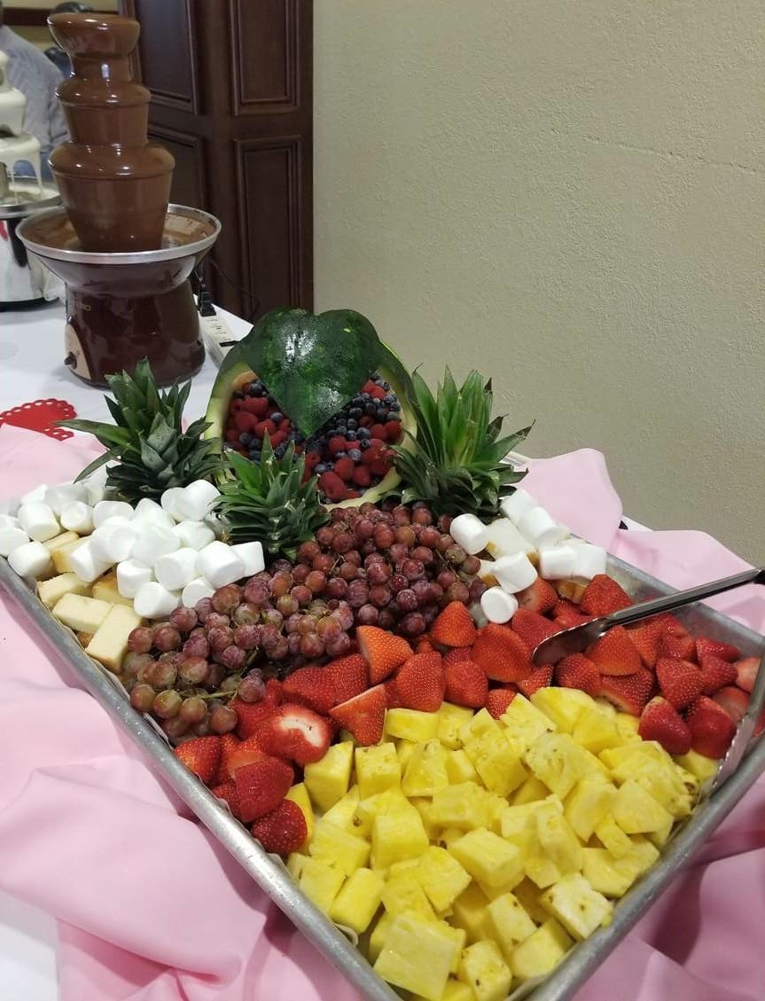 A colorful fruit tray with a variety of fruits and marshmallows next to a chocolate fountain.