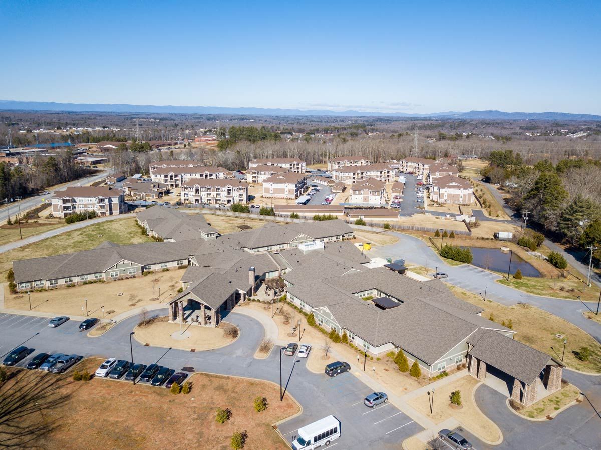 Aerial view of a suburban residential area with buildings, roads, and vehicles visible.