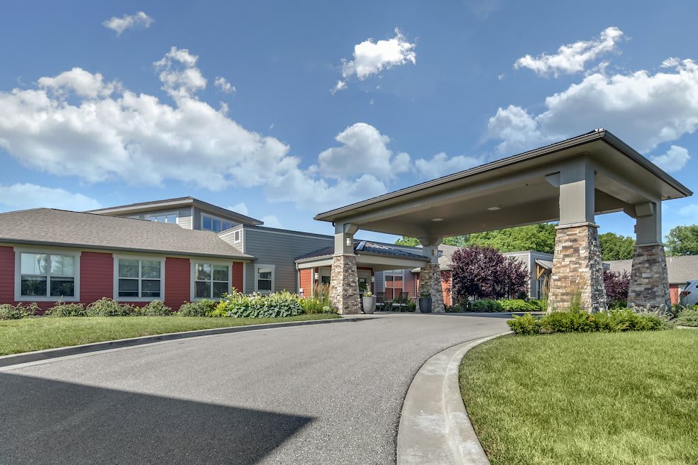 A modern building with a covered driveway and landscaped surroundings under a partly cloudy sky.