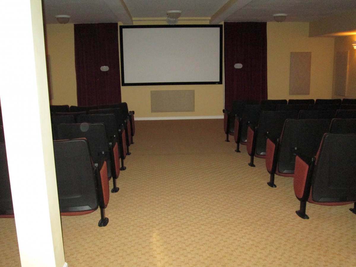 An empty movie theater with rows of seats facing a large screen.