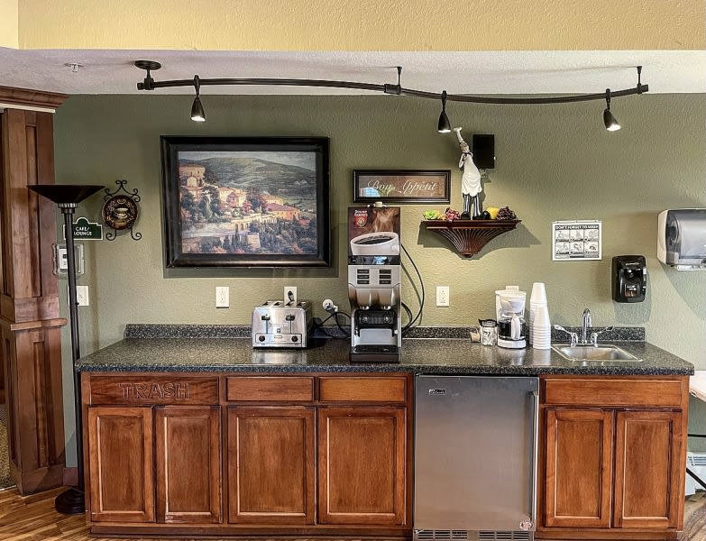 A cozy kitchen corner with a coffee station, featuring appliances, wooden cabinets, and decorative artwork.