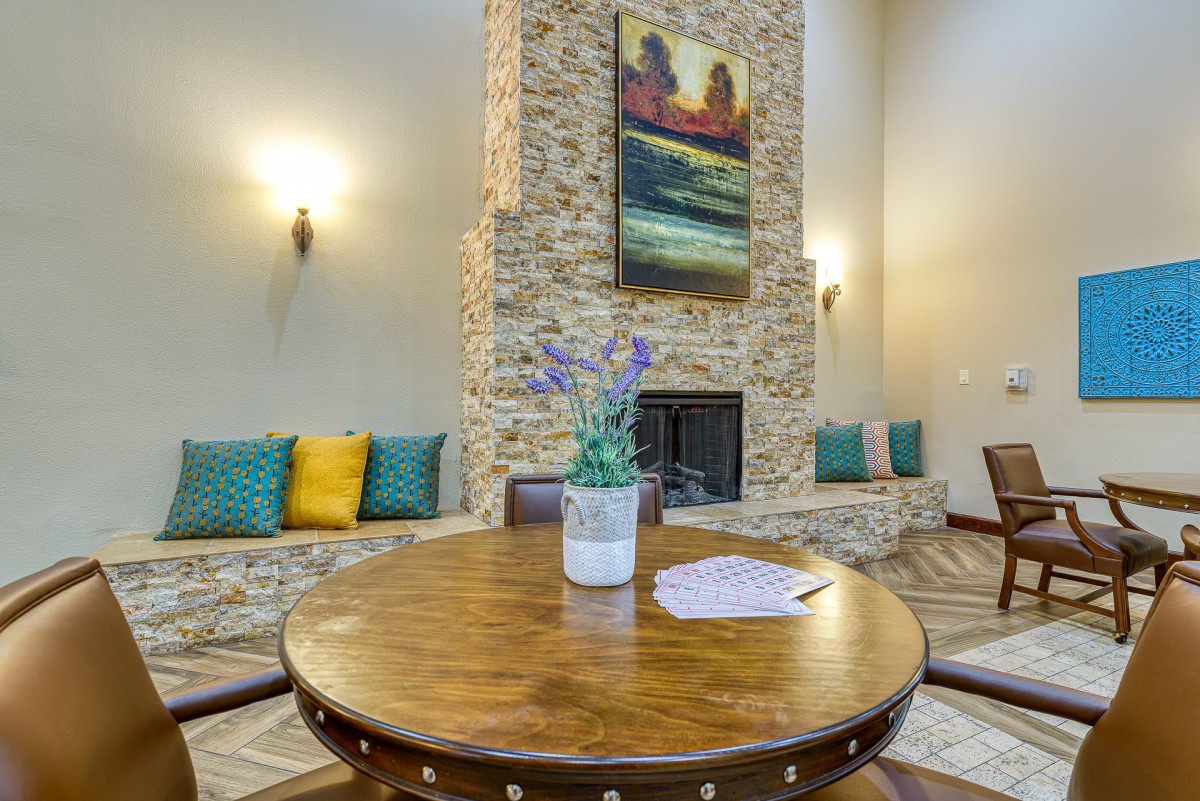 A cozy living room featuring a stone fireplace, round wooden table, and colorful decorative pillows.