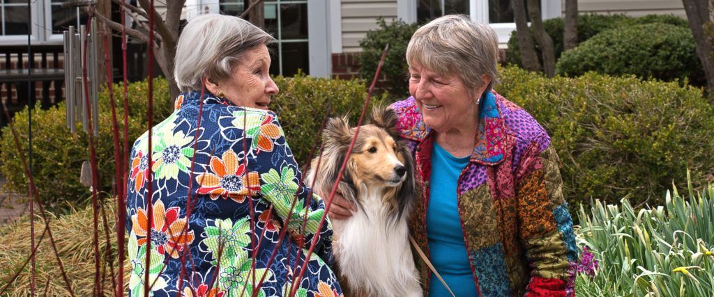 Two elderly women smiling with a dog outdoors.