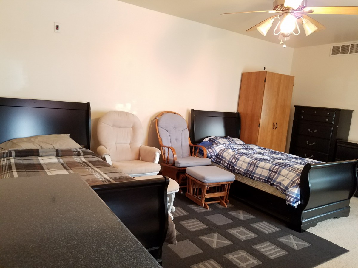 A neatly arranged bedroom featuring a single bed, armchairs, and wooden furniture.
