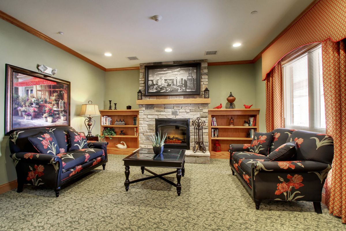 A cozy living room featuring a central fireplace, surrounded by comfortable furniture and bookshelves.