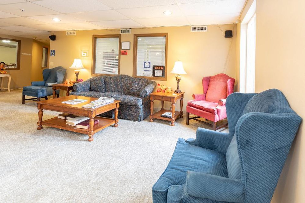 A cozy living room with sofas, armchairs, and a coffee table, warmly lit by lamps.