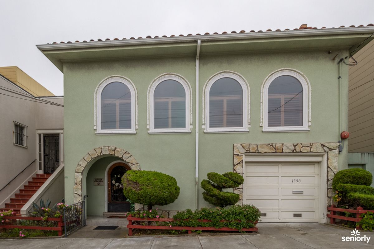 A two-story house with arched windows and a green exterior, featuring a garage and well-maintained landscaping.