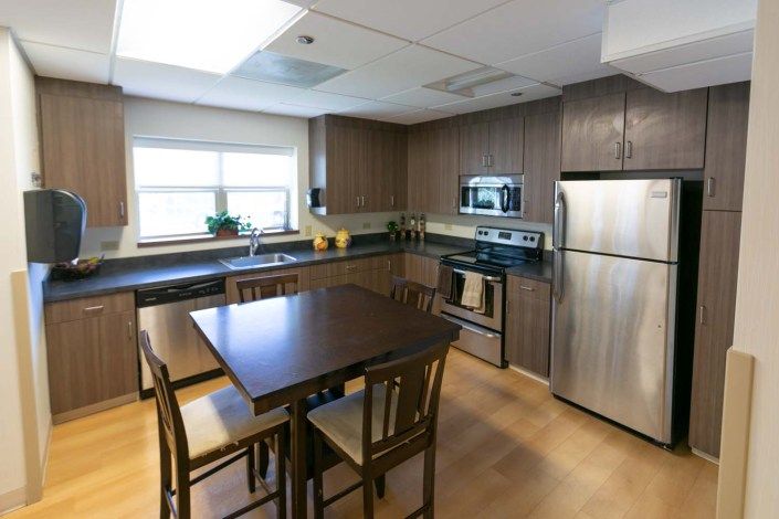 A modern kitchen featuring wooden cabinets, stainless steel appliances, and a dining area with a table and chairs.