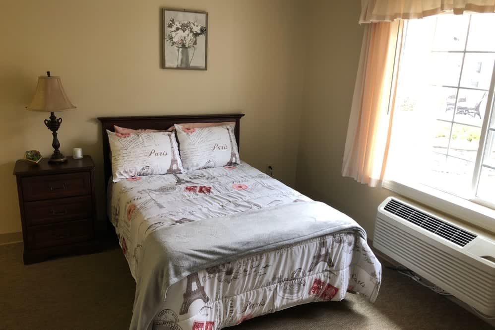 A cozy bedroom with a neatly made bed, featuring floral bedding and natural light from the window.
