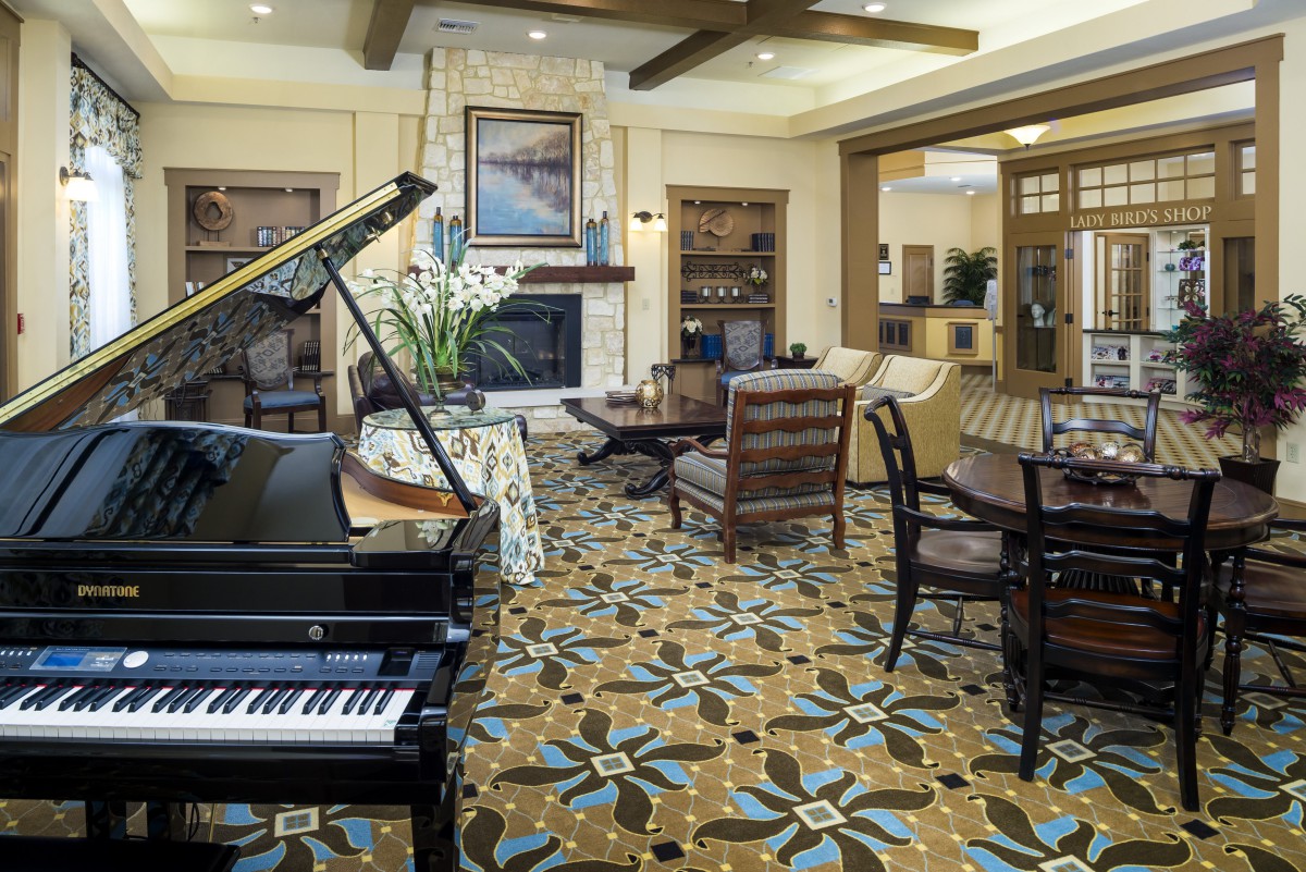 A spacious living room featuring a grand piano, elegant furniture, and a patterned carpet.