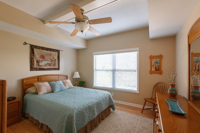 A cozy bedroom featuring a bed with blue bedding, a ceiling fan, and natural light from the window.