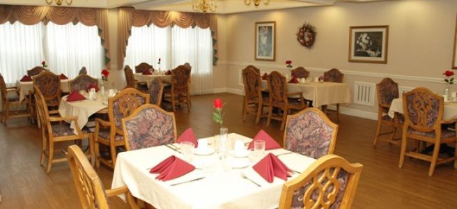 An elegantly set dining area with wooden chairs and red napkins.