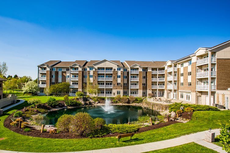 A modern apartment complex featuring landscaped gardens and a central pond with a fountain.