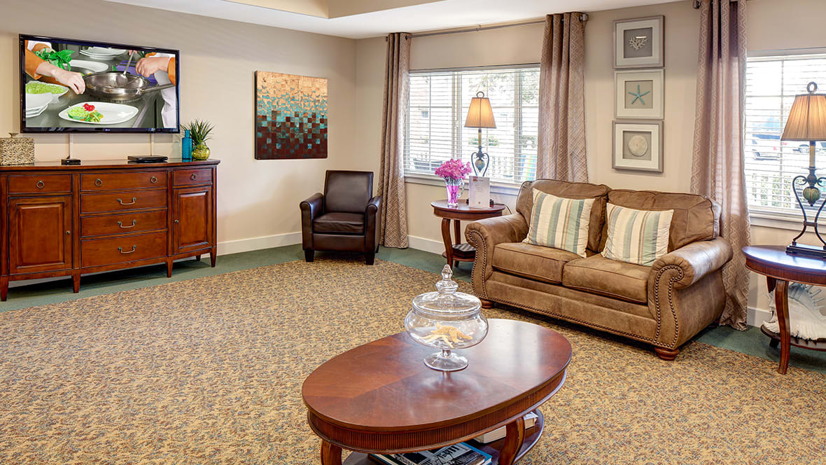 A cozy living room with a sofa, armchair, and wooden coffee table, featuring elegant decor and a large window.
