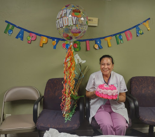 A joyful birthday celebration in a hospital setting, featuring a smiling individual holding a cake surrounded by festive decorations.