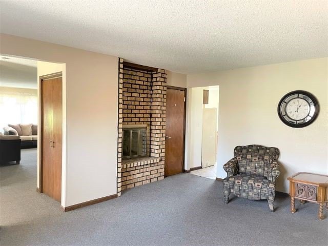 A living room with a brick fireplace, carpeted floor, and a patterned armchair near a wall clock.