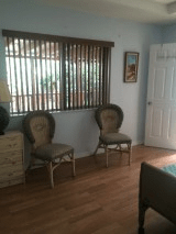 A cozy room with two chairs, a lamp on a dresser, and a window with blinds.