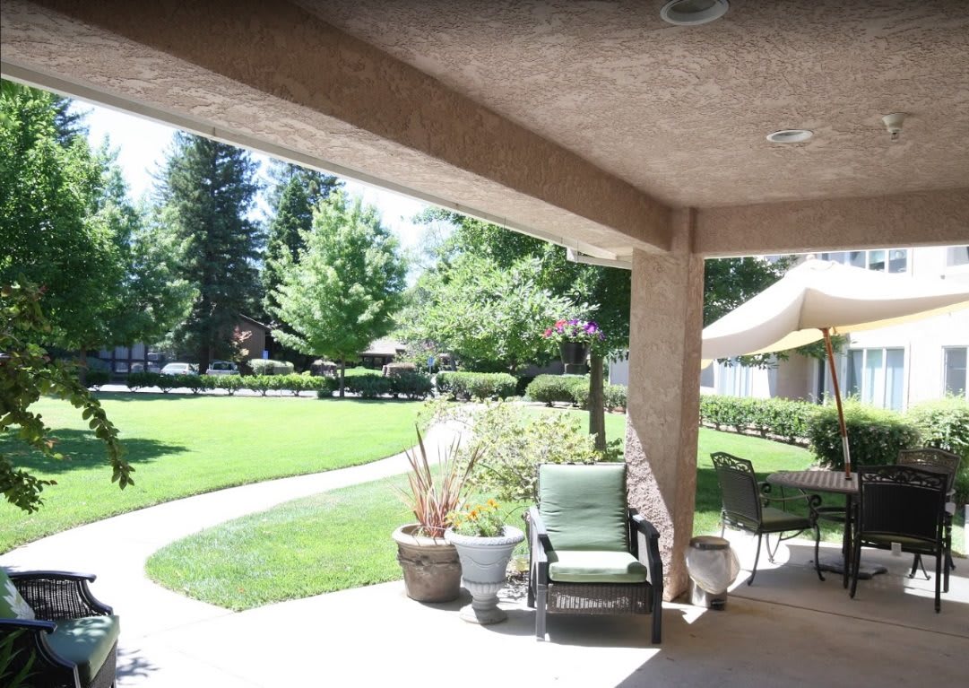 A sunny patio with outdoor seating overlooking a lush green lawn.
