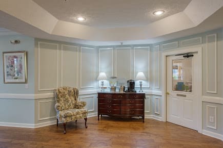 A traditionally decorated room with paneling, featuring a floral armchair and a wooden cabinet under soft lighting.