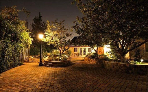 A serene garden illuminated by soft lights at night, featuring a cozy house in the background.