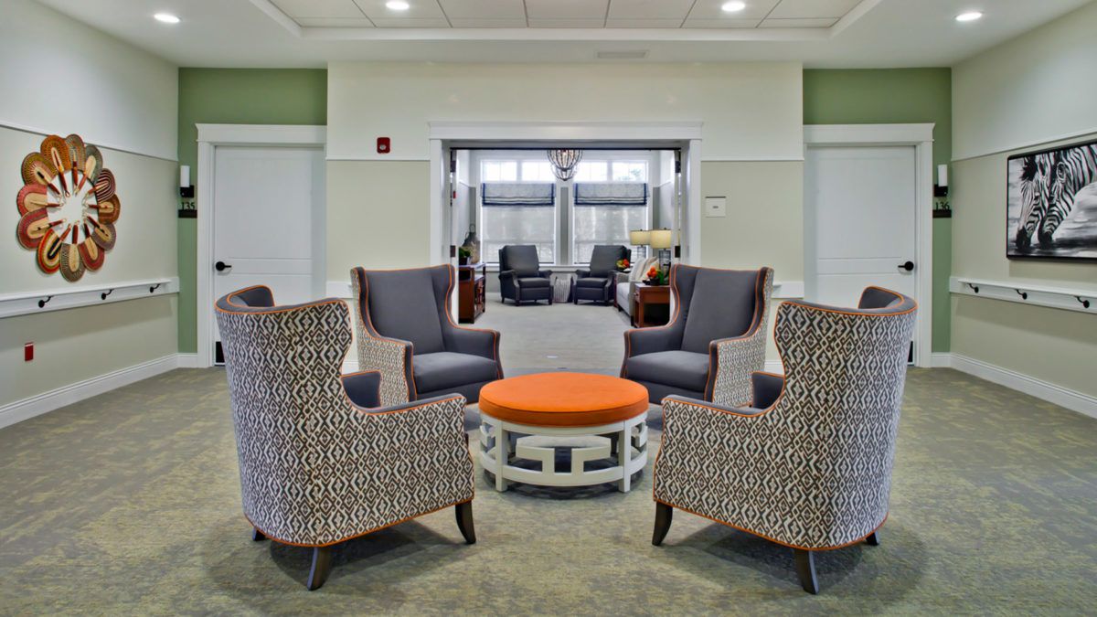 A modern seating area with four upholstered chairs and an orange ottoman in a lobby setting.