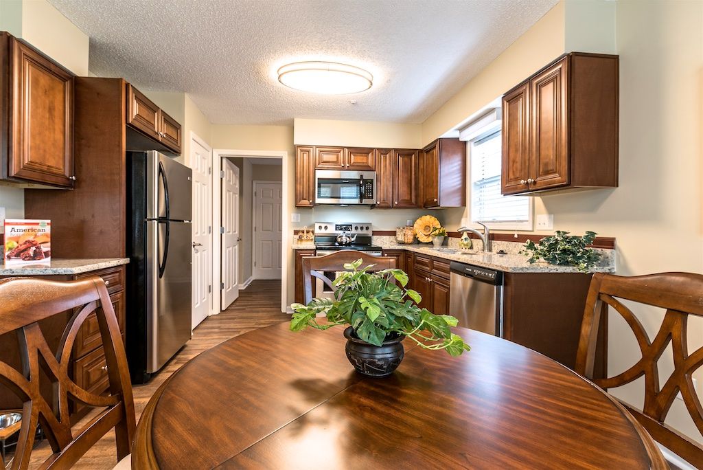 A cozy kitchen with wooden cabinets and stainless steel appliances, featuring a dining table with a houseplant centerpiece.