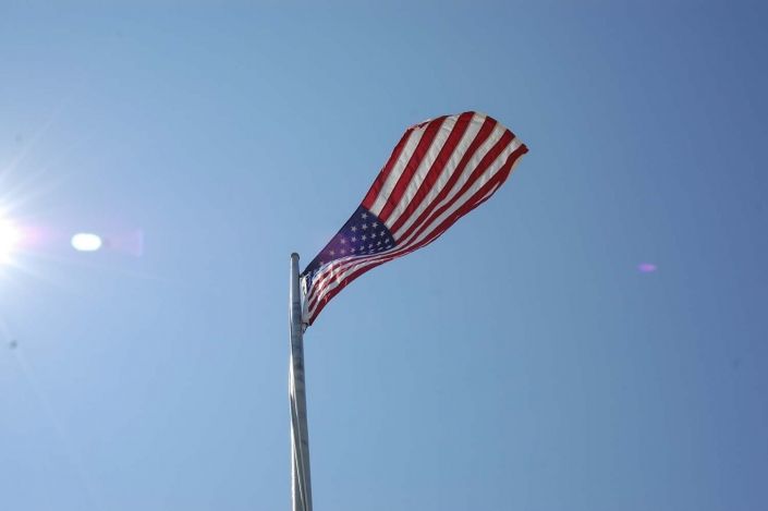 An American flag waving on a flagpole against a clear blue sky.
