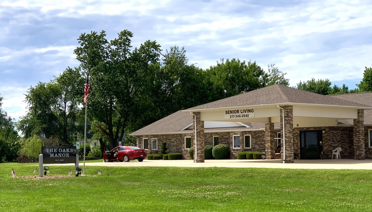 A small bank building surrounded by trees and greenery with a parked car nearby.