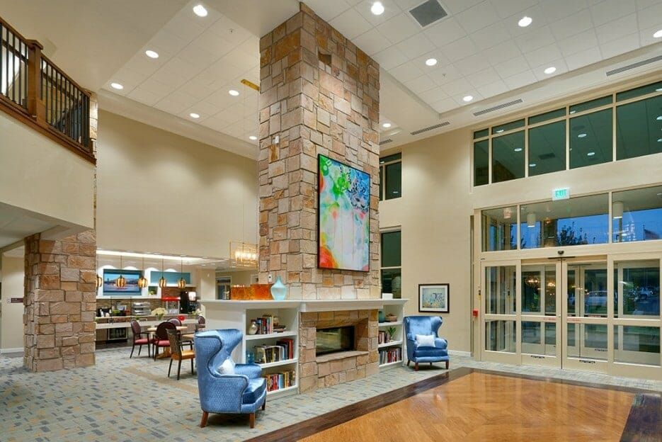 A modern and spacious lobby featuring a central fireplace with armchairs and colorful artwork.