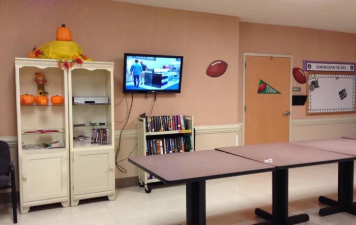 A cozy community center TV room with books, a mounted television, and tables for activities.