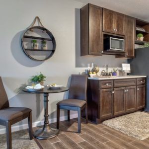 A cozy kitchen corner with a small dining area, featuring dark wooden cabinetry and shelving.