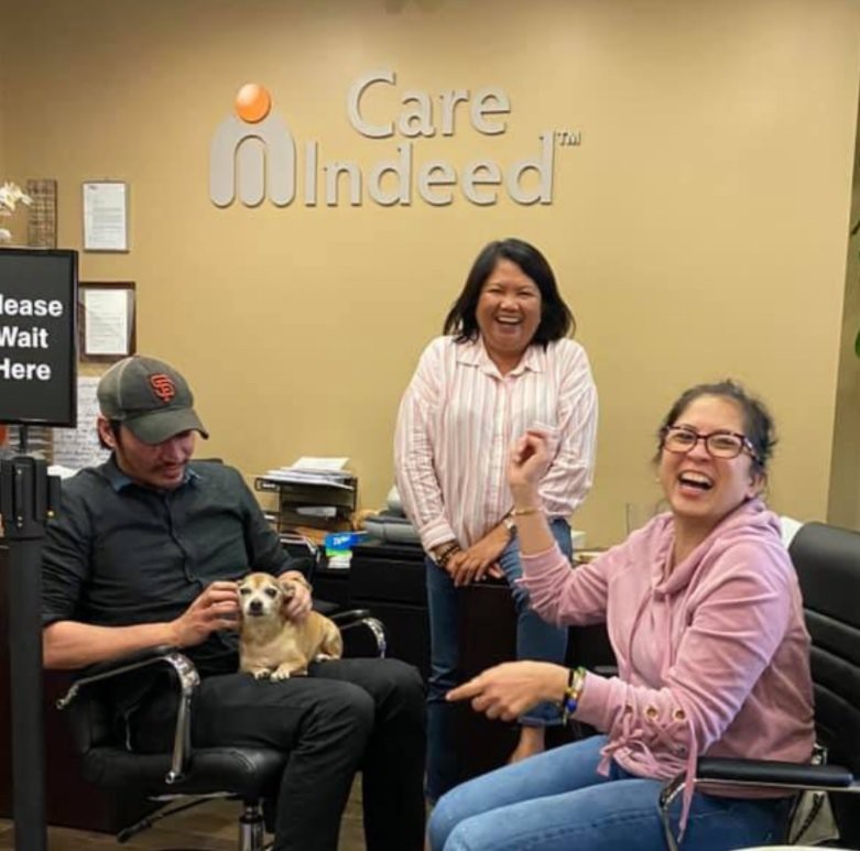 Three people in an office enjoying their time with a small dog.