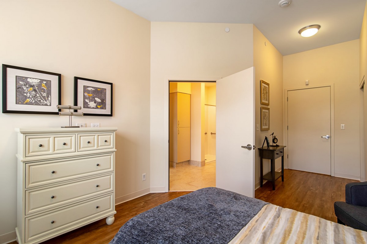A cozy bedroom featuring a dresser, artwork, and an open doorway.
