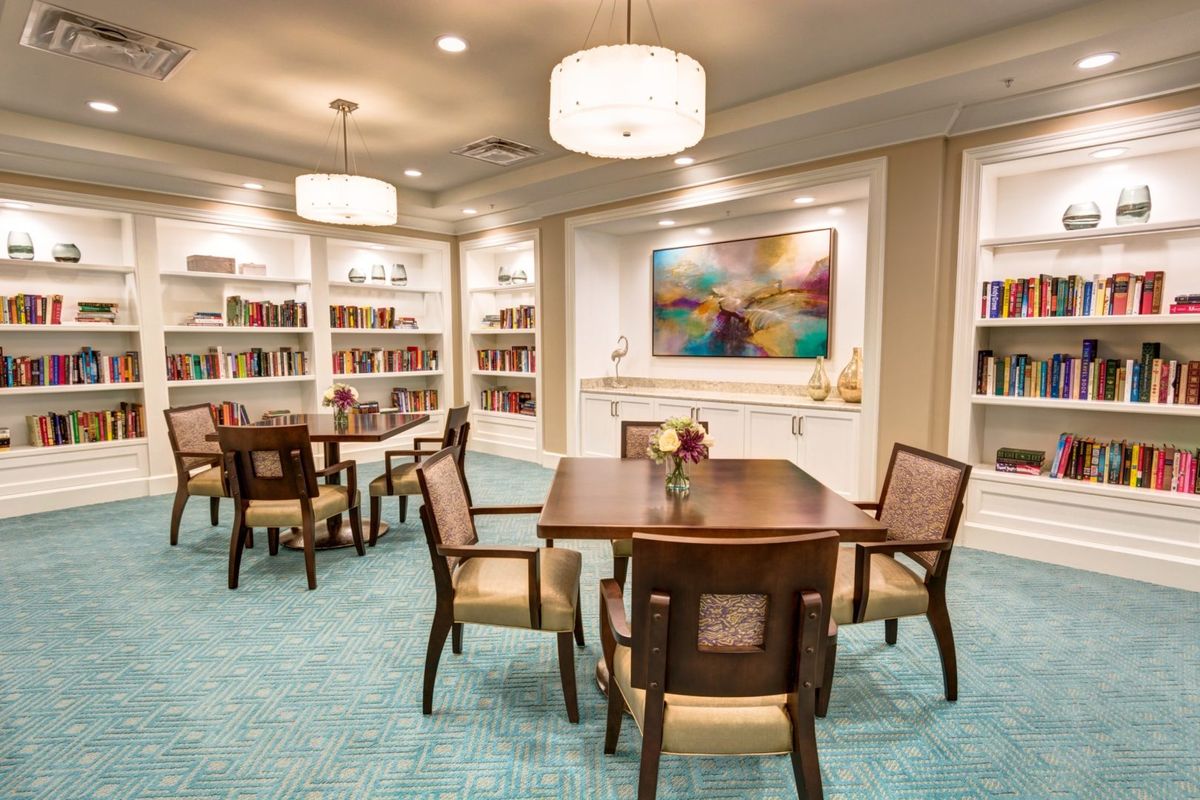 A cozy library interior with tables and chairs, surrounded by bookshelves and warm lighting.