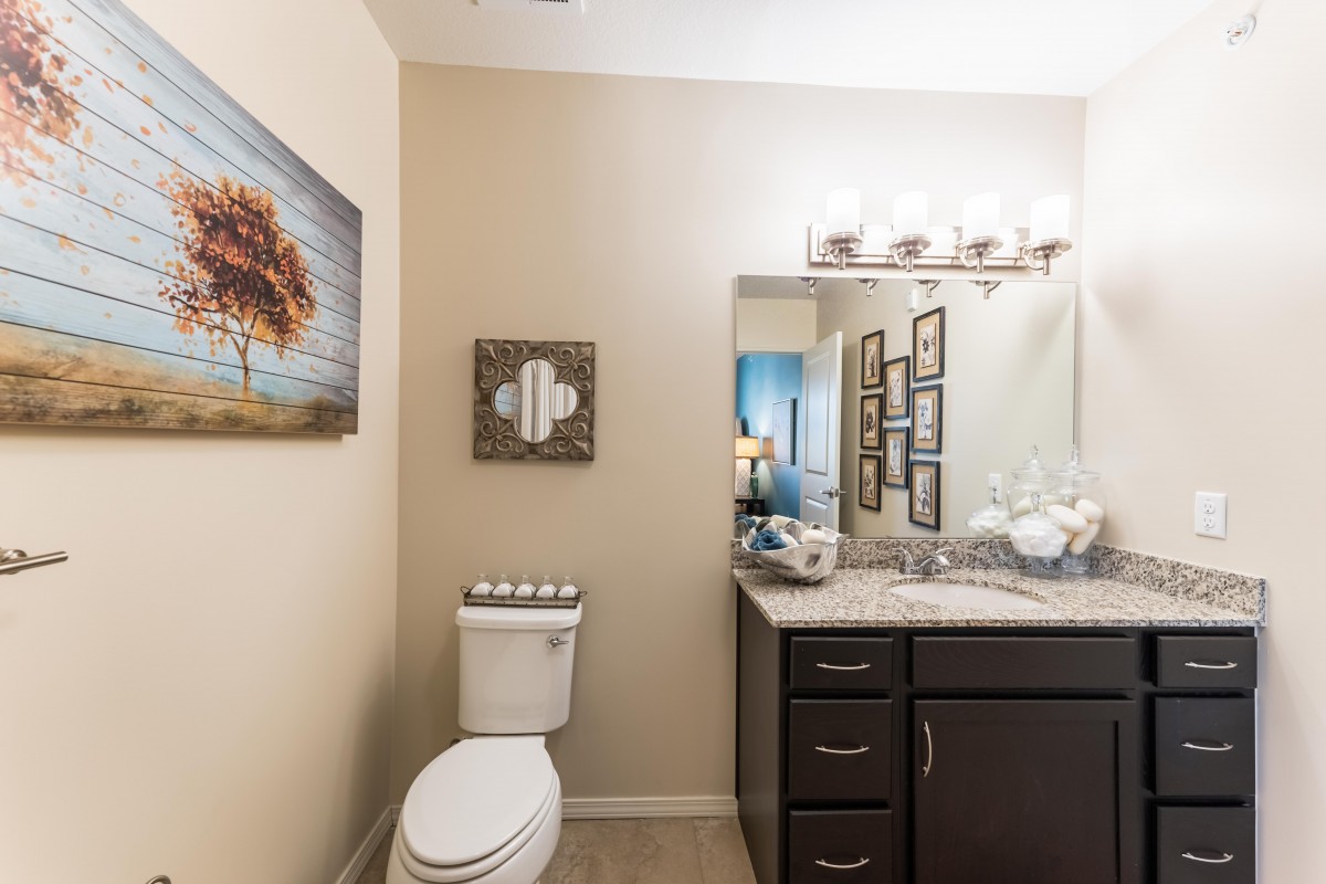 A well-lit bathroom featuring a toilet, sink, mirror, and wall decorations.