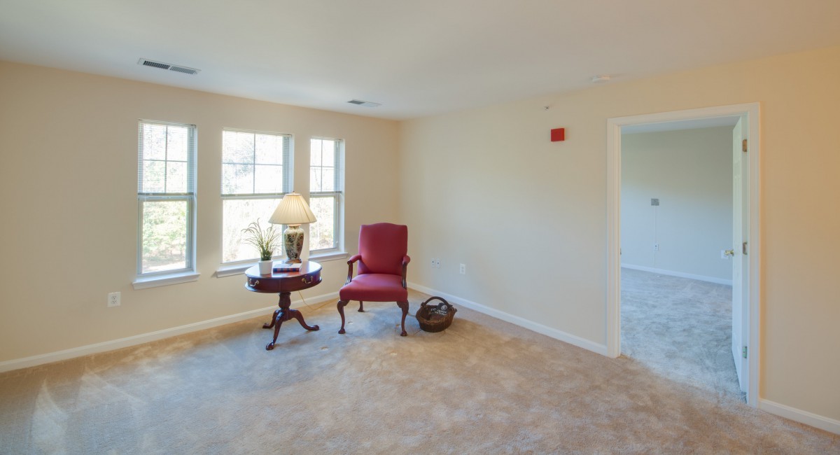 A cozy living room with a red chair, side table, and a lamp by the window.