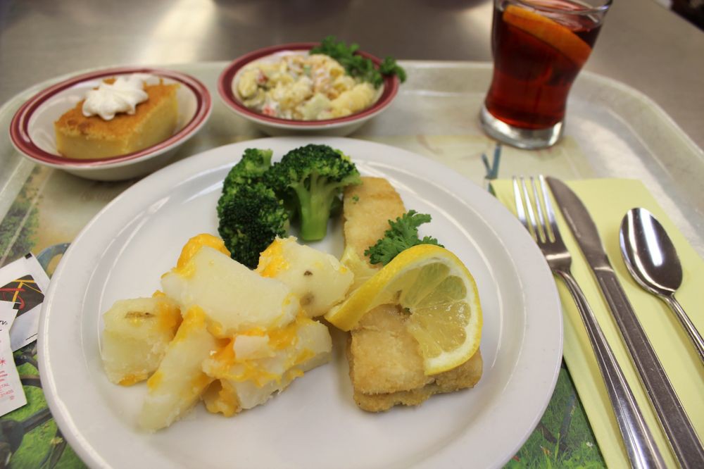 A meal featuring fish with lemon, broccoli, and potatoes, accompanied by coleslaw and a drink.