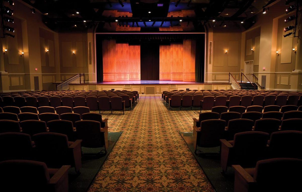 An empty theater auditorium with rows of seating facing a stage with closed curtains.