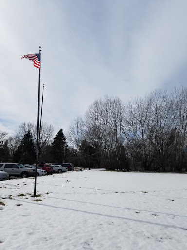 A snowy landscape featuring a flagpole with the American flag standing proudly amid leafless trees.