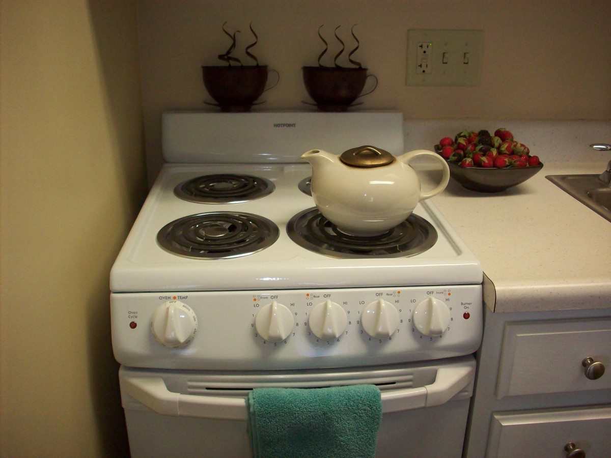 A kitchen stove with a teapot on the burner and a bowl of strawberries nearby.
