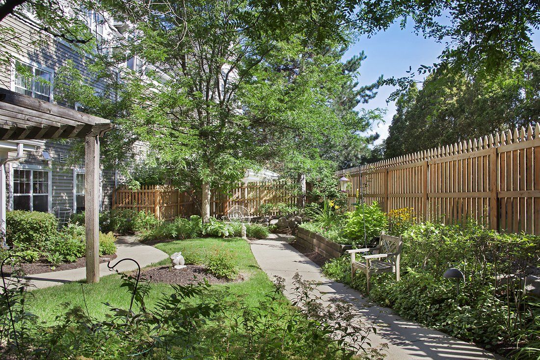 A serene garden with a winding pathway, surrounded by lush greenery and enclosed by a wooden fence.
