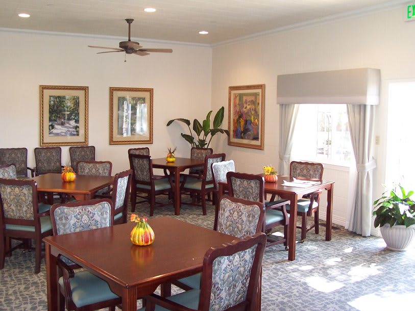 A neatly arranged dining area with multiple tables and chairs, decorated with artwork and plants.