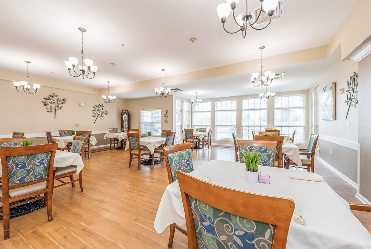 A spacious, well-lit dining room with multiple tables and chairs, adorned with elegant chandeliers and large windows.