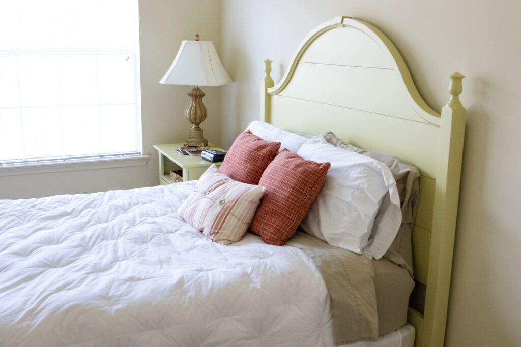 A cozy bedroom setting with a neatly made bed, decorative pillows, and a lamp on the nightstand.
